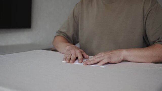 Medium shot slightly above table level showing an adult man aligning a paper airplane on the table. Camera emphasizes symmetry of wings and controlled finishing movements. High quality 4k footage