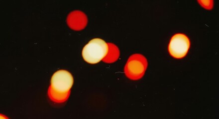 Abstract image featuring out of focus red and yellow bokeh lights on a dark background with subtle dust