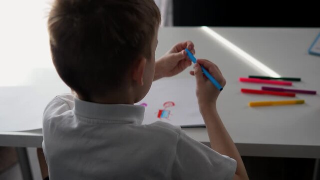 Close-up of a young boy writing or drawing with a pencil at a desk at home or school. Child focused on learning and doing homework. Concept of education, childhood development, concentration