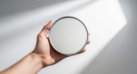 Person holding a small round hand mirror against a minimalist white background