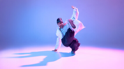 Street dancer performing high kick in studio with colorful lighting. Concept of flexibility training, dance technique, powerful movement, modern choreography visuals, and urban performance.
