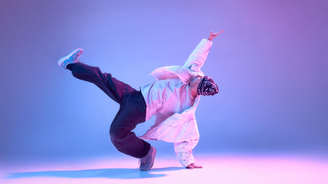 Male hip hop dancer balancing on one hand with extended leg in studio. Concept of advanced dance technique, strength training, urban choreography, physical control and creative discipline.