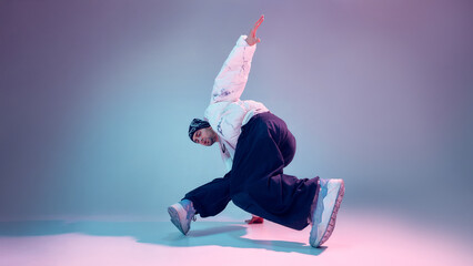Obraz premium Breakdance dancer performing floor balance move in studio with gradient light background. Concept of street dance training, body control, flexibility, modern choreography, and youth culture.