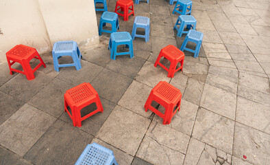 Fototapeta premium A collection of plastic stools in red and blue placed on the paving stone outdoors