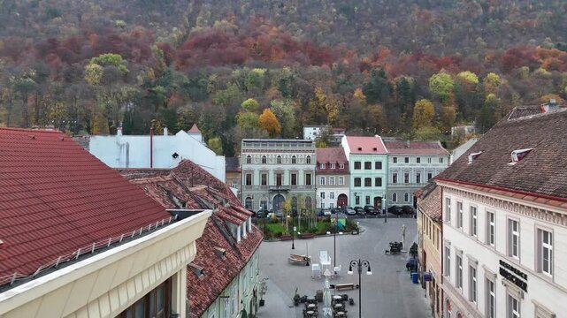 Brașov, Romania. Forward drone in street between buildings, rooftops towards hill with forest, trees in autumn colors, brasov city. Touristic must-see destination.