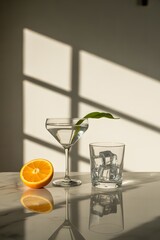 Refreshing Still Life: Martini glass with a green leaf, ice-filled tumbler, and orange slice on a marble surface.