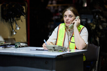 Worker on the phone at a desk, taking notes in a warehouse setting