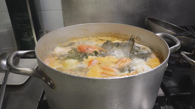 Rustic sea bass and shrimp broth boiling with herbs in a cooking pot