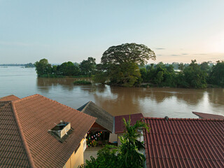 Naklejka premium View over village rooftops toward a wide river and trees in Don Det, Laos, during soft evening light.