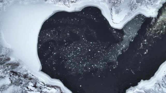 Aerial view of a partially frozen river with snow-covered banks, the icy water reflecting the sky's muted tones, Ruka, Pohjois-Pohjanmaa, Finland.