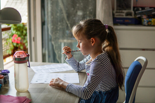 Nine year old schoolgirl doing homework at desk in her room, elementary education concept