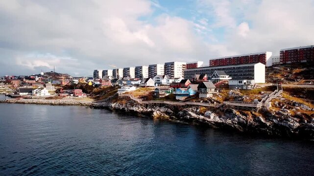 Aerial drone view over the rugged coastline of Nuuk City, Greenland, panning right at low angle, Arctic urban shoreline, clear daylight atmosphere, captured on 9 June 2024