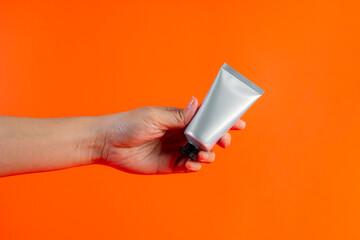 Cosmetics tube against and hand on orange background. 