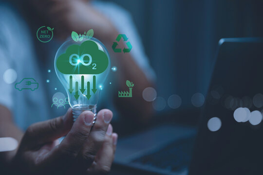 Hand of a man holding a light bulb with a glowing cloud of CO2 with green eco icons.