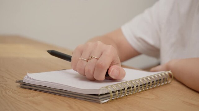 Woman hand repetitively clicking pen top over notebook paper at desk. Concept of nervous habit, anxiety or compulsive behavior during work or study. Original sound of clicking is included.
