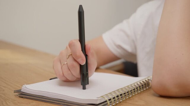 Woman hand hitting pen top on notebook paper at wooden desk. Concept of writer block, frustration or thinking process during business or education. Original sound of tapping hits is included.