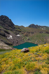 A lake in the mountains, natural scenery, green meadows, snow-capped mountains, blue sky, winter season. Lake views in bloom in spring. Hakkari Cilo Sat Lakes. A lake view in the mountains. 