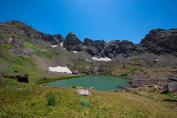 A lake in the mountains, natural scenery, green meadows, snow-capped mountains, blue sky, winter season. Lake views in bloom in spring. Hakkari Cilo Sat Lakes. A lake view in the mountains. 