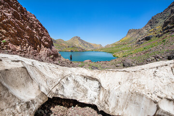 A lake in the mountains, natural scenery, green meadows, snow-capped mountains, blue sky, winter season. Lake views in bloom in spring. Hakkari Cilo Sat Lakes. A lake view in the mountains. 