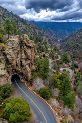 Scenic Mountain Road Winding Through Lush Greenery and Rocky Cliffs with a Dark Tunnel Entrance Under a Cloudy Sky