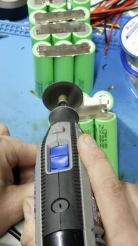 Electrician hand cuts metal plate connecting batteries with mini saw device in shop closeup. Technician separates power elements cluster at workplace vertical shot