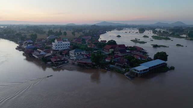 Aerial view of Don Det village beside the river, showing clustered houses, boats, channels, and distant hills.