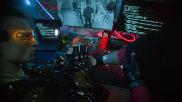 Tracking shot of young woman with shaved head showing her arm to cyberpunk man in LED visor scanning code while programming and monitoring CCTV footage on computer in neon workspace