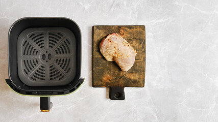 Chicken leg on a wooden cutting board beside an air fryer basket