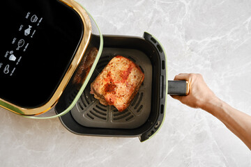 A hand removes an air fryer basket with roasted piece of pork fillet