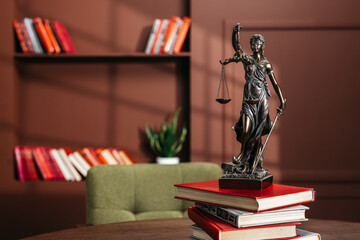 Lady Justice statue holding scales and sword, positioned on a stack of red books on a wooden table, with a bookshelf and green plant in a modern interior setting © wedmoments.stock