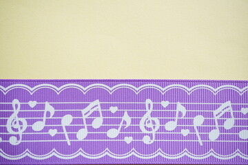 音符とハート模様がデザインされた紫色のリボンを黄色の背景に配置した写真。音楽や子ども向けデザイン、可愛らしいイメージに使いやすい、明るくポップな背景素材。