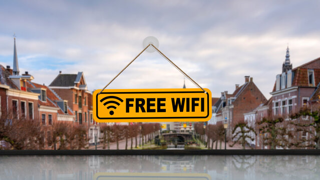 Yellow sign with Free Wifi text hanging on a window. Blurred historic city background with old houses and cloudy sky. Concept of internet connectivity, travel, and hospitality services