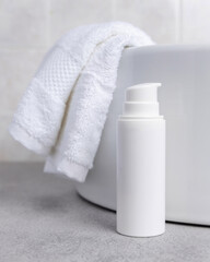 White cosmetic pump bottle on grey stone near white bath towel and basin close up, mockup