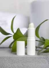 White blank cream tube against green leaves on grey stone in white bathroom, mockup