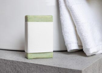 Green soap bar with blank label near white bath towels and basin on grey stone, mockup