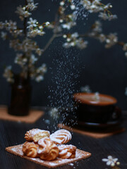 Assorted pastries on wooden plate with powdered sugar falling in dark setting. Concept of food background with copy space for bakery branding, menu design, banner, social media.