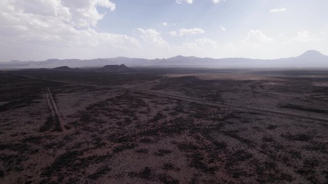 Aerial drone shot of a desolate desert highway with low mountains in the background