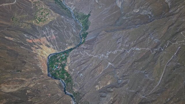 High-altitude drone shows the immense scale of Colca Canyon as famous hiking trail winds through the oasis and climbs out the other side highlighting one of Peru&rsquo;s most iconic trekking destinations.