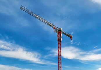 Crane construction work takes place under blue sky during the daytime with clouds in the background