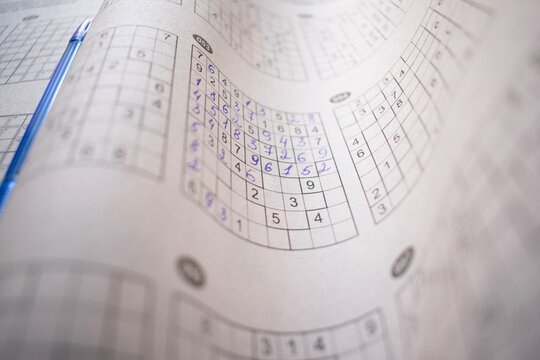 Curved paper pages of a sudoku puzzle book with completed number grids and a blue pen