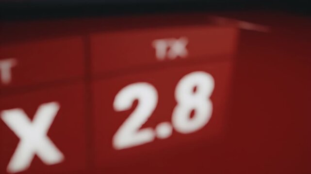 Blurred Numbers on Red Background - This video shows a blurred view of white numbers, "1X" and "2.8", printed on a red surface, possibly part of a sign or display.