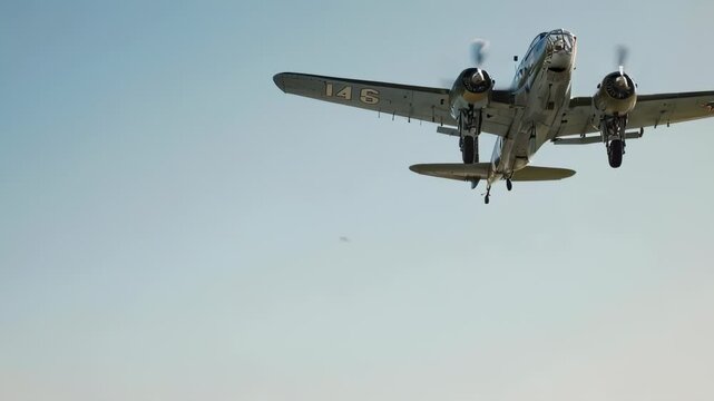 A vintage, twin-engine aircraft soars through the clear, azure sky