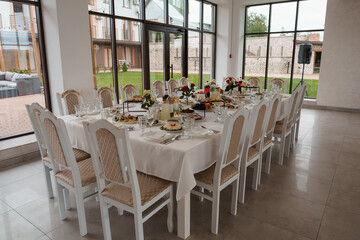 Elegant White Table Setting with Floral Arrangements in Modern Glass-Walled Dining Room with Outdoor Garden View