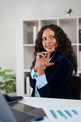 Confident female executive at her desk in a modern office, smiling and gazing into the distance...