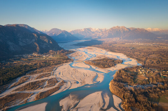 Aerial view of the braided river carving through the landscape, framed by the majestic mountains under the soft glow of the rising sun, Friuli Venezia Giulia, Italy.