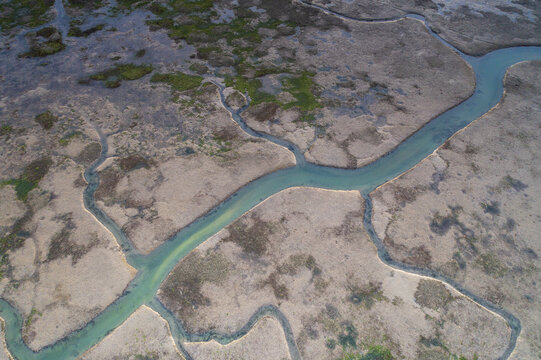 Aerial view of meandering turquoise streams cut through the muddy, textured earth, creating a stark contrast between land and water, Friuli Venezia Giulia, Italy.
