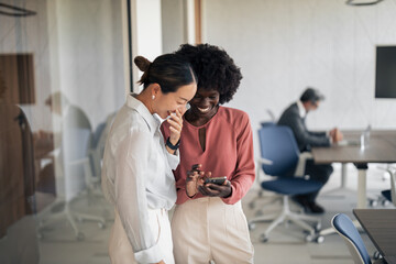 Diverse businesswomen laughing at smartphone in office