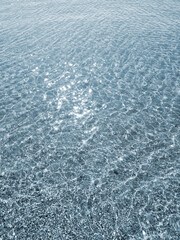 Clean transparent water on shallow sandy seashore with shells with shells on sunny summer day. Sun glare on surface of water. Small waves on sea coast. Nature backdrop. Natural background