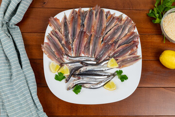 Raw and fresh anchovies with lemon and parsley on a white plate. Flat lay.