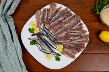 Raw and fresh anchovies with lemon and parsley on a wooden table. Flat lay.